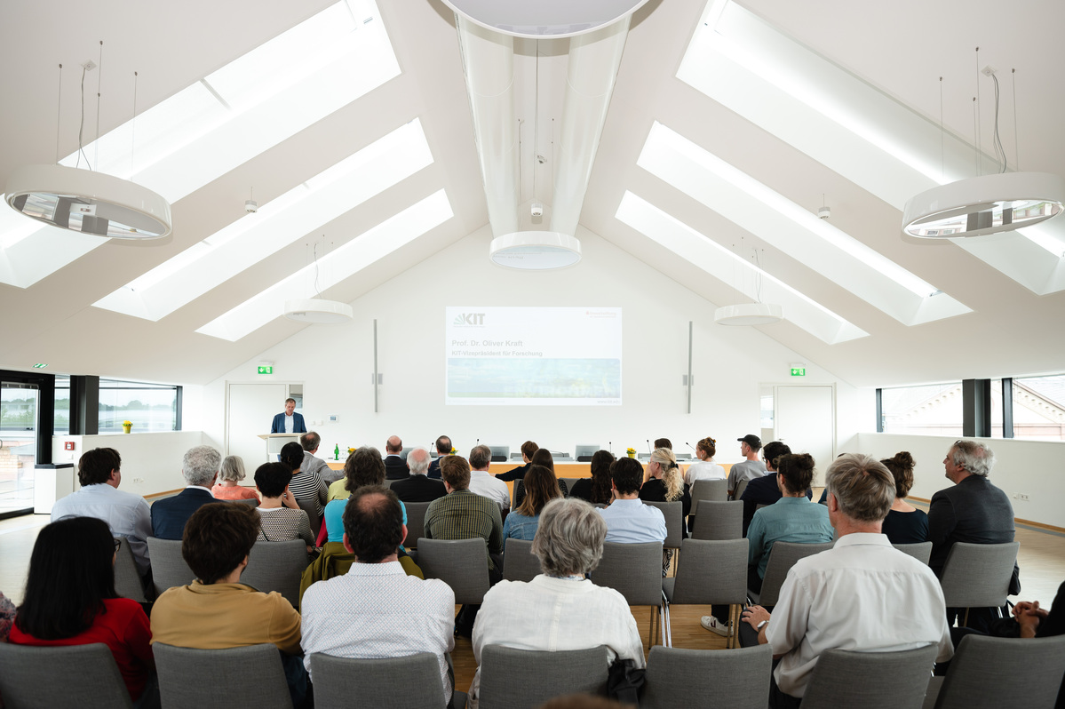 etwa 20 Menschen von hinten, im Hintergrund wird ein Vortrag mit Präsentation gehalten
